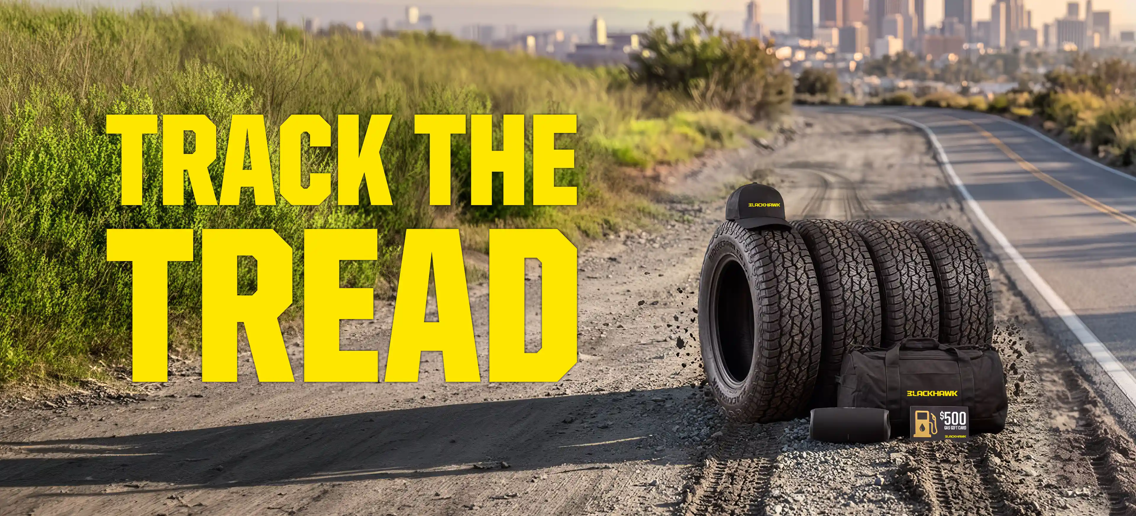 Promotional banner featuring the headline "TRACK THE TREAD" in large yellow lettering over a rugged dirt road leading toward a distant city skyline. On the right, four Blackhawk all-terrain tires are displayed alongside a Blackhawk-branded cap, duffel bag, rolled mat, and a $500 gas gift card. Tire tracks run through the foreground, reinforcing the off-road theme.